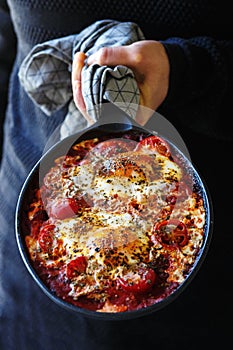 Shakshouka - Middle eastern traditional dish with poached eggs in tomato sauce, man holding pan