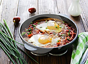 Shakshuka or fried eggs in tomato sauce with red bell pepper in a serving cast-iron frying pan on a wooden background