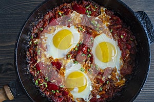 Shakshuka, fried eggs with tomatoes, onion, red pepper and spices in cast iron pan