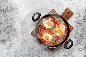 Shakshuka in a frying pan on a gray rustic background. Poached eggs in a spicy tomato pepper sauce. Typical Jewish or