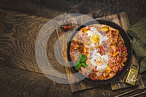 Shakshuka in an iron pan on wooden background