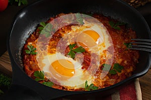 Shakshuka from two eggs in tomato sauce with fresh tomatoes, spices and herbs in a black frying pan. Close-up scrambled