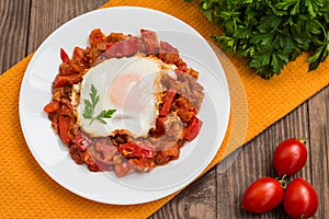 Shakshuka on a white plate. Traditional Jewish dish. Wooden table. Top view. Close-up