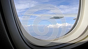 Shaky handheld video of airplane wing through porthole, blue sky with clouds. View of passenger on airplane flight in