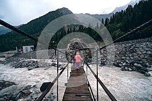 A shaky wooden bridge with metal cables. Stormy flow of a mountain river. Active recreation and hiking. Gloomy rainy weather.