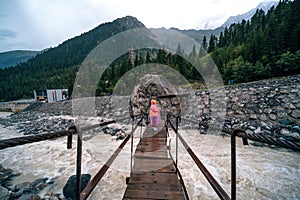 A shaky wooden bridge with metal cables. Stormy flow of a mountain river. Active recreation and hiking. Gloomy rainy weather.