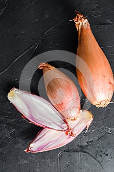 Shallot, eschalot or scallion raw ripe onions sliced and halved black background top view close up vertical