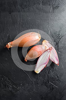 Shallot, eschalot or scallion raw ripe onions sliced and halved black concrete textured background top view close up vertical