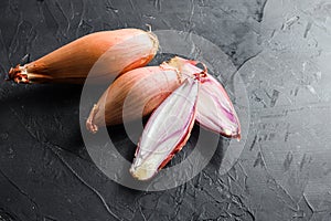 Shallot, eschalot or scallion raw ripe onions sliced and halved black concrete textured background top view space for text