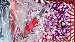 shallots in a container are in the process of peeling the skin using a rusty cutting knife