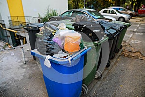 Shallow depth of field image with plastic garbage bins filled with household waste near a block of flats