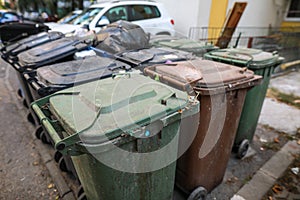 Shallow depth of field image with plastic garbage bins filled with household waste near a block of flats