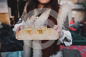 Shallow depth of field selective focus image with a woman holding a wooden plate with palinca or tuica, romanian traditional