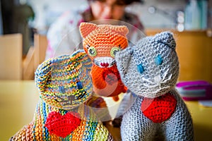 Shallow depth of field of three knitted stuffed toy cats with red hearts, woman sitting in the background.