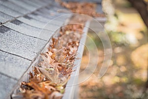 Shallow DOF clogged gutter near roof shingles of residential house full of dried leaves