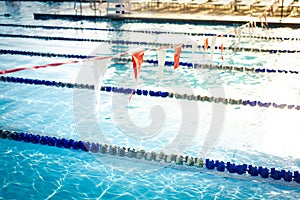 Shallow DOF string of colorful triangular backstroke flags hanging over public competitive swimming pool with pool lane divider