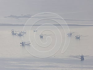 Shallow fishing boats anchor at the beach on thick fog days.