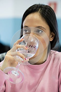 Shallow focus of a caucasian young woman drinking a glass of water against a blurred background