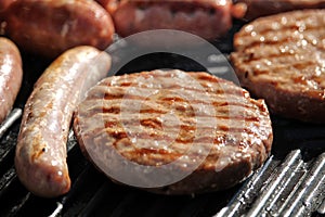 Shallow focus close up of tasty assorted delicious sausages and burgers sizzling and cooking on a barbecue griddle plate, outside