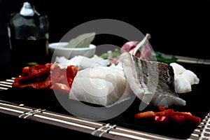 Shallow focus closeup shot of raw fish next to vegetables on a black cutting board