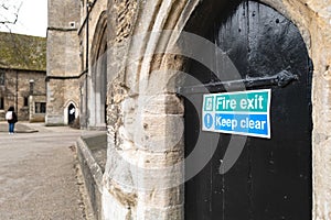 Shallow focus of a Fire Exit sign seen attached to a medieval, wooden door located at the base of a church.
