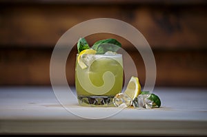 Shallow focus of a lemon basil cocktail with ice cubes and lemon on a wooden background