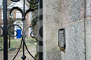 Shallow focus of a metal intercom system seen out a gated entrance to a distant large period house.