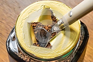 Shallow focus of a newly opened, instant coffee jar showing a tea spoon in the dried granules.