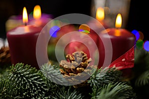 Shallow focus pine cone on advent wreath with four lit candles and decor