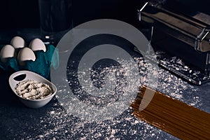 Shallow focus shot of a bowl of flour with sprinkled flour, eggs, and an uncooked pasta