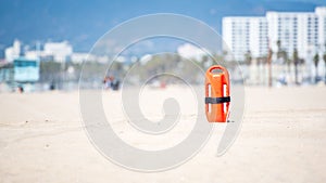 Shallow focus shot of an orange rescue buoyancy stubbed vertically in the sand.