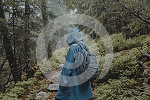 Shallow focus shot of a traveler with blue raincoat walking in a wet forest