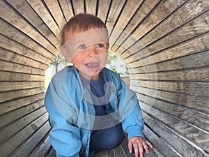 Shallow focus shot of a 2-year-old caucasian blonde baby girl in a wooden tunnel