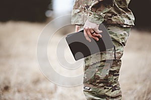 Shallow focus shot of a young soldier holding a bible in a field