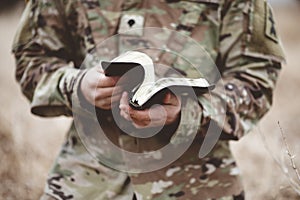 Shallow focus shot of a young soldier  holding an open bible in a field