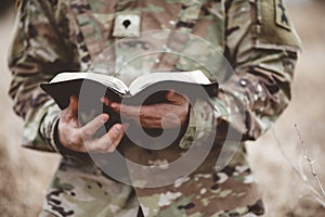 Shallow focus shot of a young soldier holding an open bible in a field