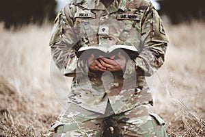 Shallow focus shot of a young soldier kneeling while holding a bible in a field