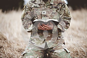 Shallow focus shot of a young soldier kneeling while holding a bible in a field photo