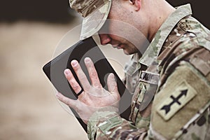 Shallow focus shot of a young soldier praying while holding the bible