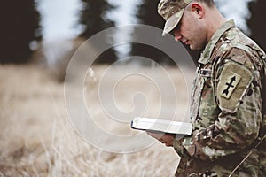 Shallow focus shot of a young soldier reading a bible in a field