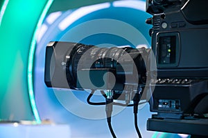 Shallow focus on a video camera lens, recording show in a TV studio with a blue theme