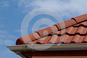 shallow zink eavestrough or gutter. red brown sandy textured modern concrete roof tiles in closeup