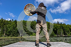 Shaman man on dock with sacred drum and stick