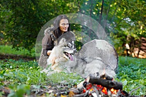 Shaman woman with an Alaskan Malamute next to the fire in the forest