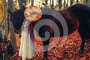 Shaman woman in autumn landscape with her horse.