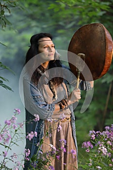 Shaman woman drumming in the evening forest