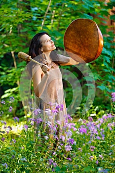 Shaman woman drumming in the forest in the daytime