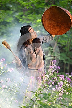 Shaman woman drumming in the forest in the rays of the setting sun