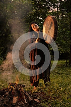 Shaman woman playing on shaman drum near large fire