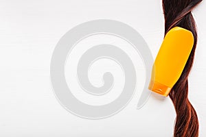 Shampoo bottle on curl strand lock of hair on white background. Orange gold mockup bottle shampoo. Flat lay with copy space. Hair